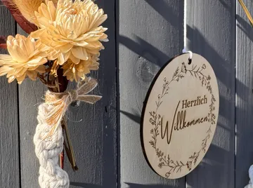Blumen und Willkommensschild an Holzwand.