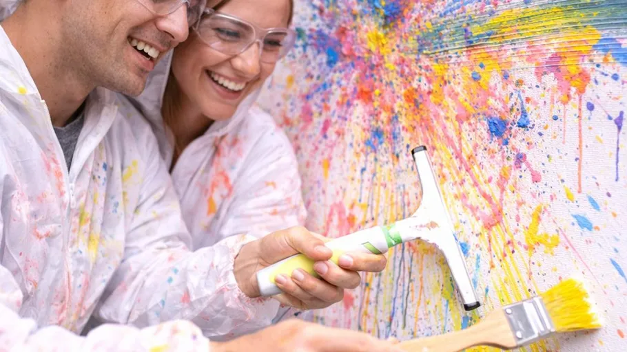 Couple joyfully painting colorful splashes on canvas.