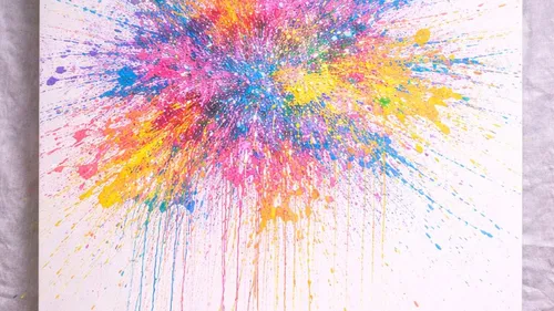 Colorful paint splatter on white canvas surface.