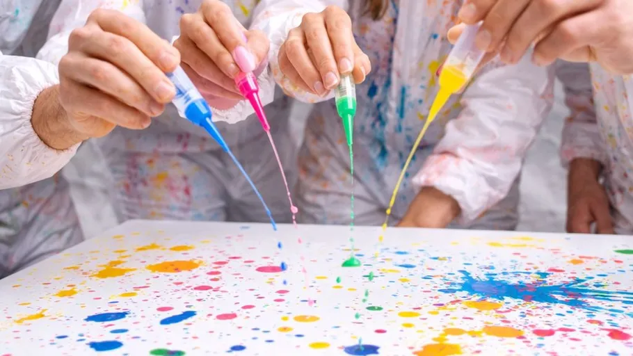 Hands splattering colorful paint with syringes.