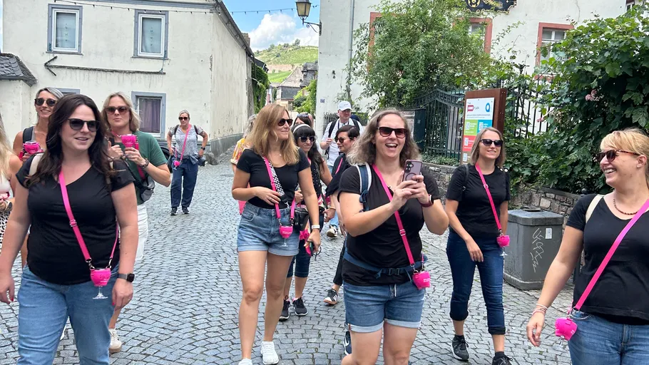 Women walking on cobblestone street holding pink cups.