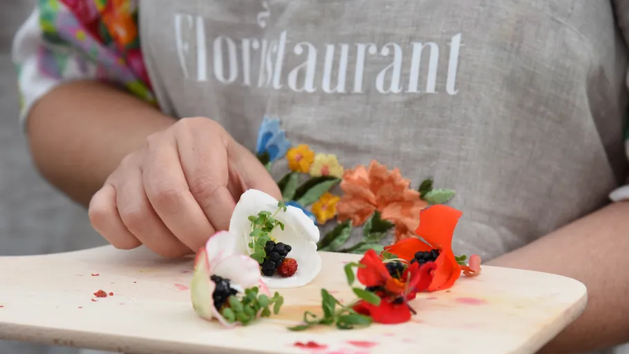 Hand arranging edible flowers and berries on tray.