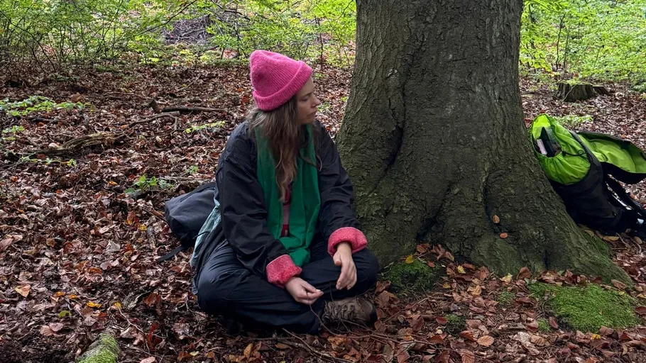 Person sitzt im Wald neben einem Baum.
