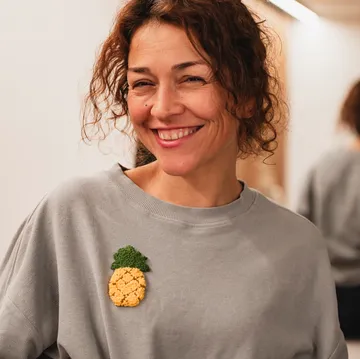 Smiling woman wearing gray sweater with pineapple patch.