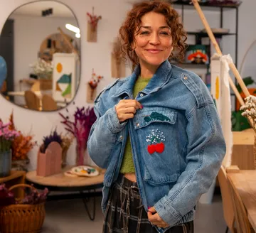 Lächelnde Frau in Jeansjacke, hält Revers, drinnen.