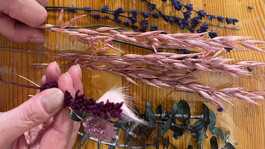 Hands arranging dried flowers on wooden table.