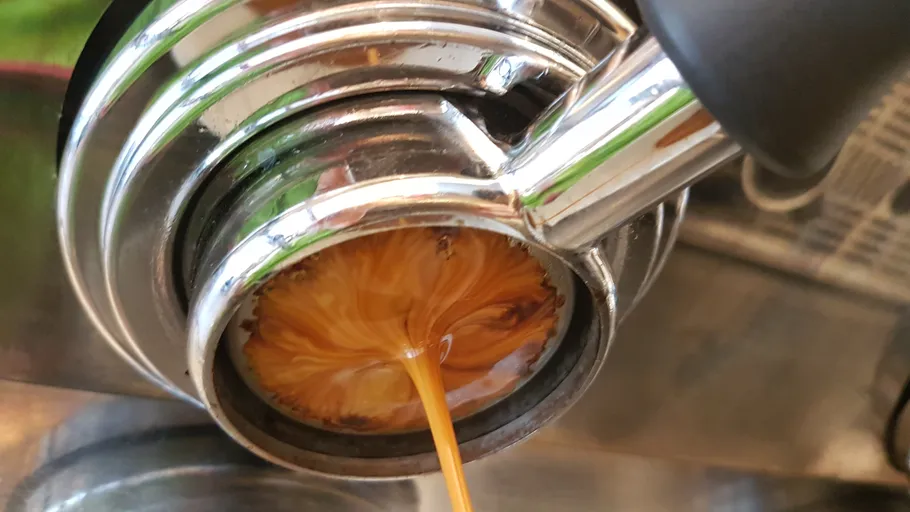 Espresso brewing from metal portafilter in machine.