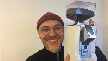 Man smiling, holding a white coffee grinder.