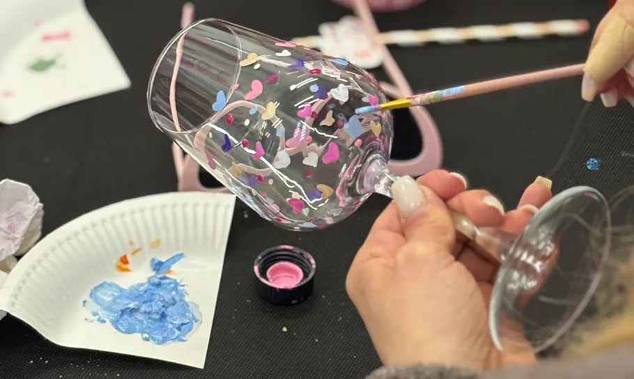 Person painting colorful hearts on a wine glass.