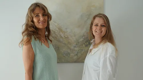 Two women smiling in front of abstract painting.