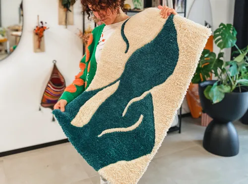 Person holds abstract-patterned rug indoors.