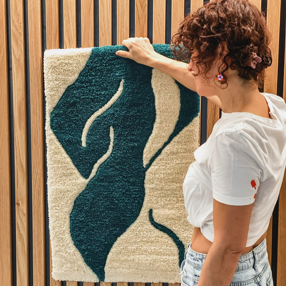 Woman adjusting abstract rug on wood wall.