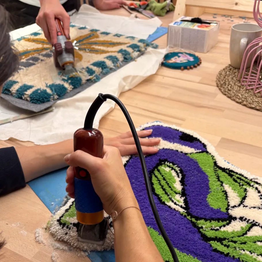 Hände tufting buntes Teppichkunstwerk auf Tisch.