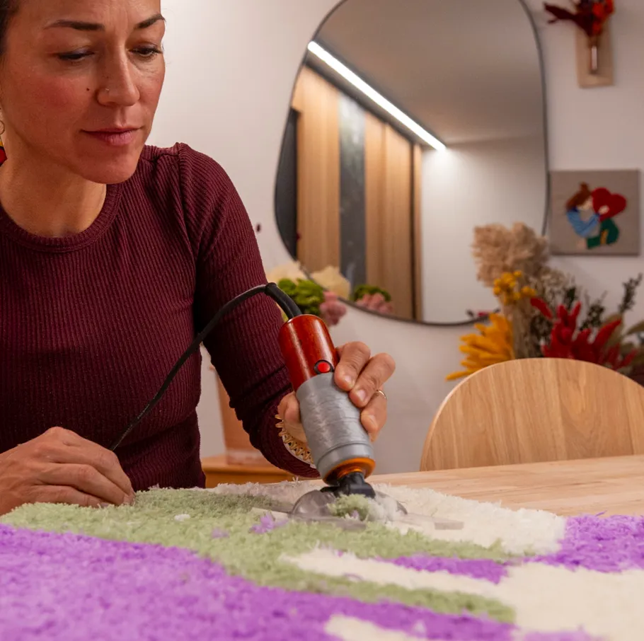 Frau arbeitet mit Tufting-Werkzeug an buntem Teppich.
