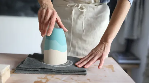 Person shaping pottery with hands on table.