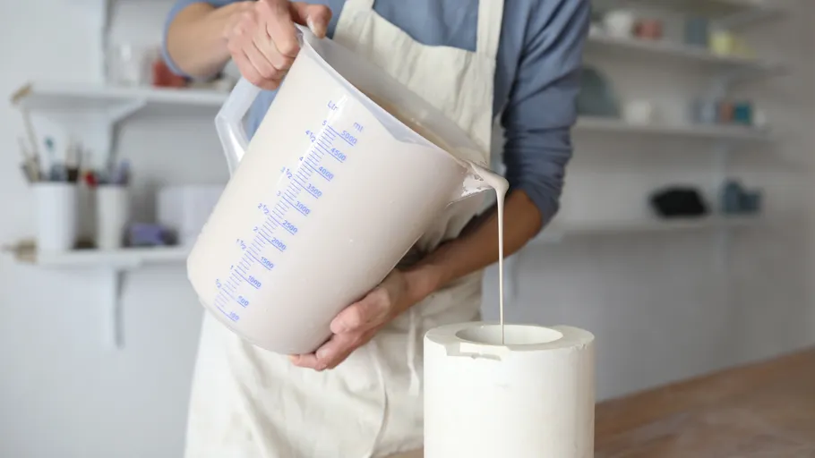 Person pouring liquid into mold in workshop.