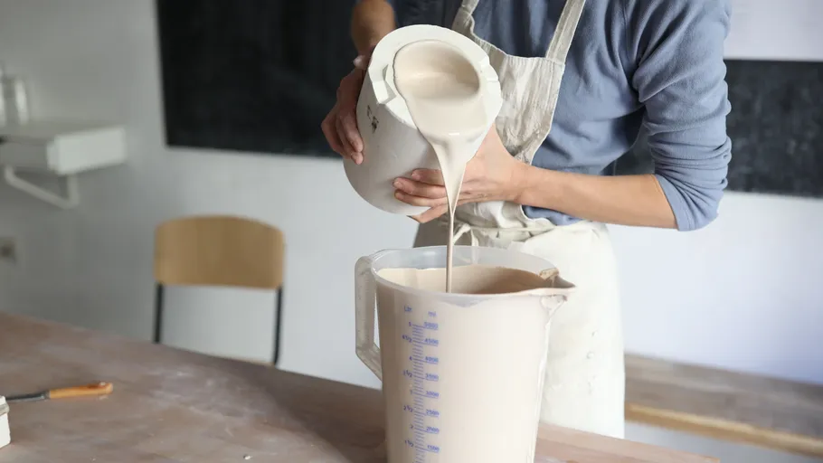 Person pouring white liquid into measuring jug.
