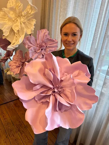 Frau hält große rosa Papierblumen drinnen.