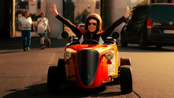 Woman driving small vintage car joyfully.