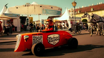 Person driving orange hotrod in city square.