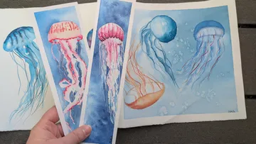 Hand hält Aquarellquallenbilder im Freien.