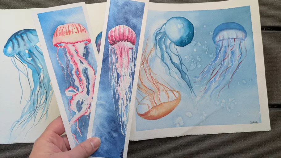 Hand holding watercolor jellyfish paintings outdoors.