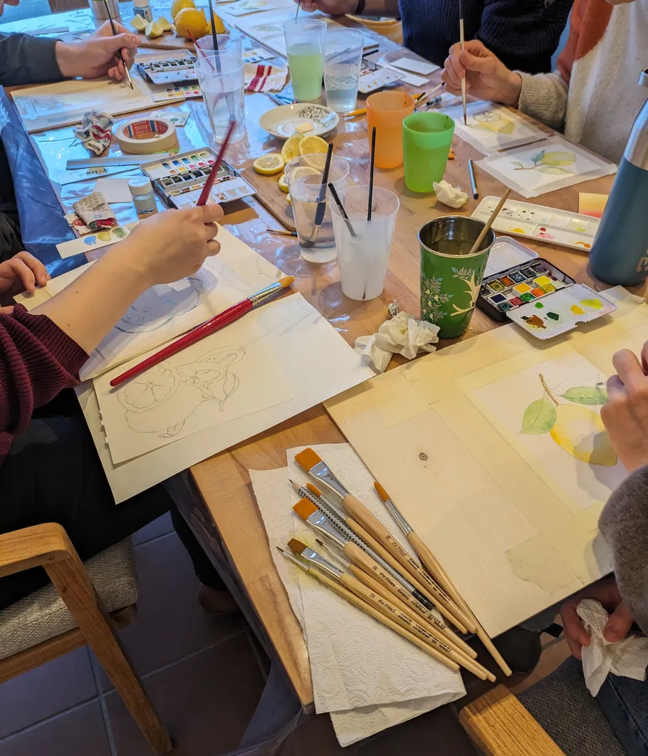 People painting watercolor fruit at wooden table.