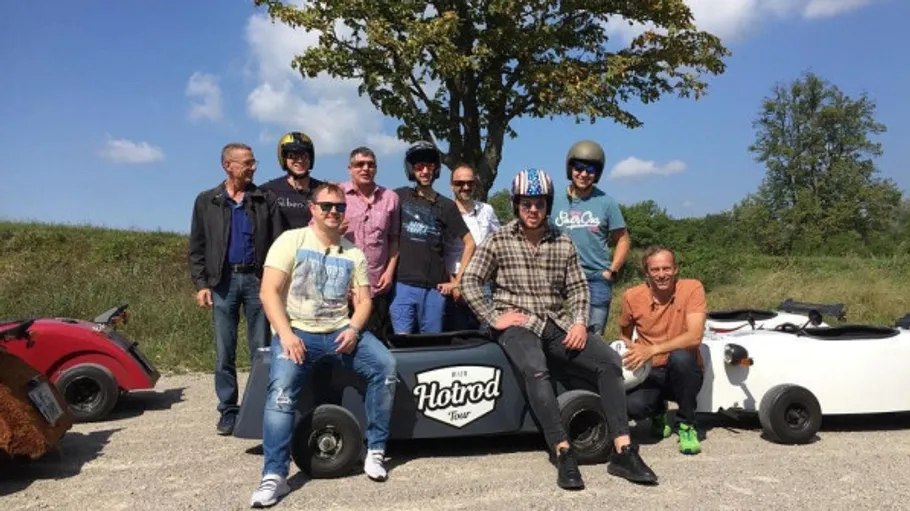 Group posing with mini hotrod vehicles outdoors.