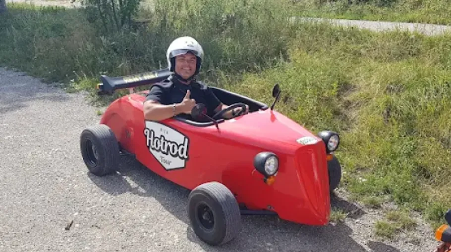 Man driving a small red hot rod outdoors.
