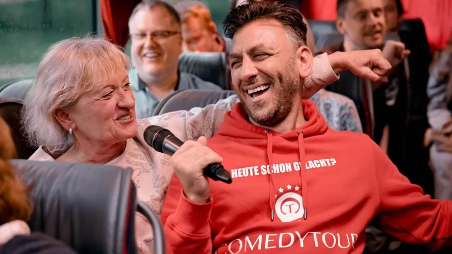 Man laughing on bus holding microphone.