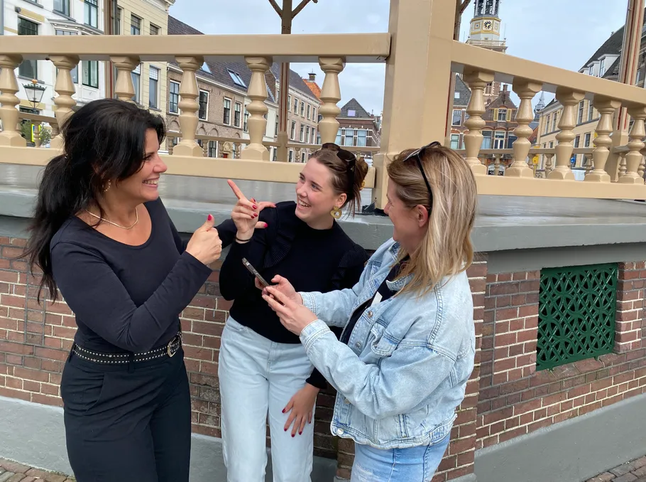 Three women smiling, talking, and gesturing outside.