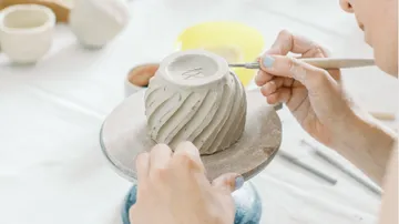 Person schnitzt Tonbecher auf Töpferscheibe.
