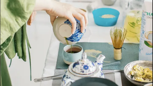 Hand pours tea into cup, surrounded by utensils.