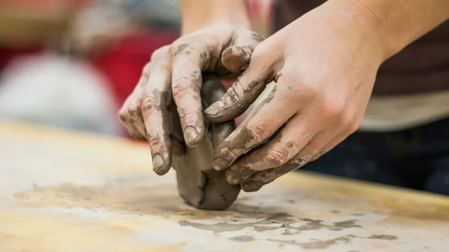 Hands shaping clay on a wooden table.