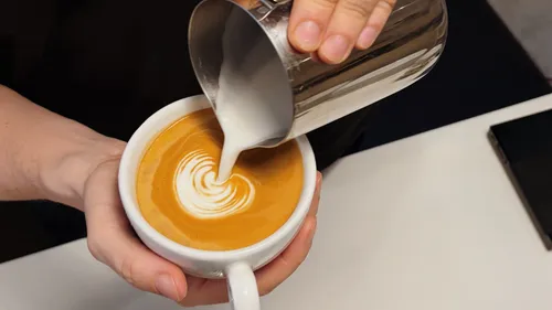 Hands pour milk art into coffee cup.