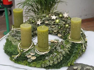Grüner Adventskranz mit vier Kerzen auf einem Tisch.