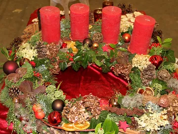 Runder Adventskranz mit roten Kerzen und Dekorationen.