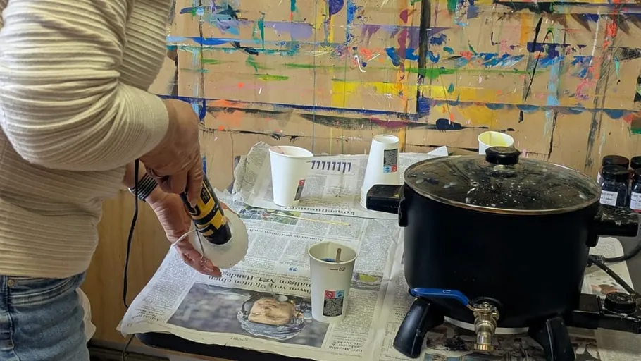 Person using power tool near paint-splattered wall.