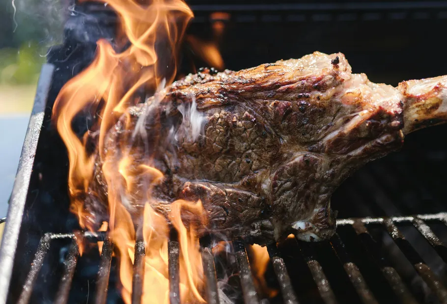 Steak cooking on a grill with flames.