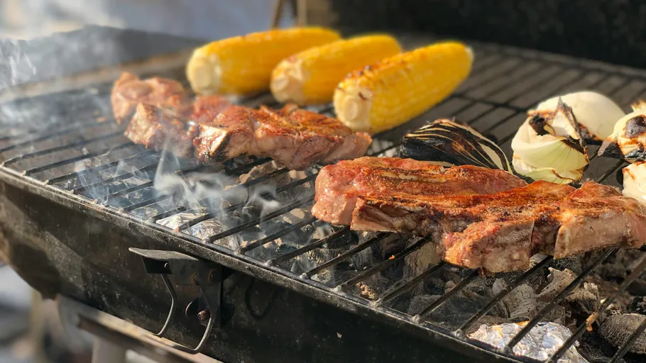 Steaks and vegetables grilling on barbecue outdoors.