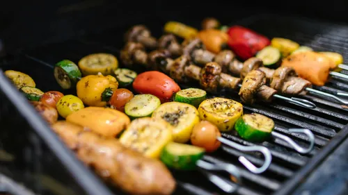 Colorful vegetables grilling on skewers outdoors.