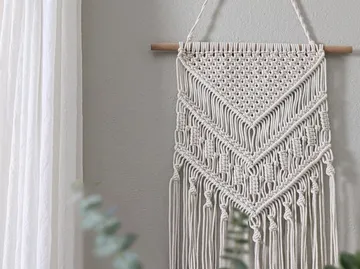 Macramé-Wandbehang an grauer Wand.