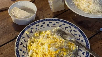 Plate of scrambled eggs with cheese, wooden table.