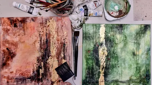 Two abstract paintings with art supplies around.