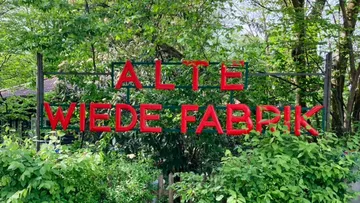 Rotes Schild mit 'Alte Wiede Fabrik' im Wald.