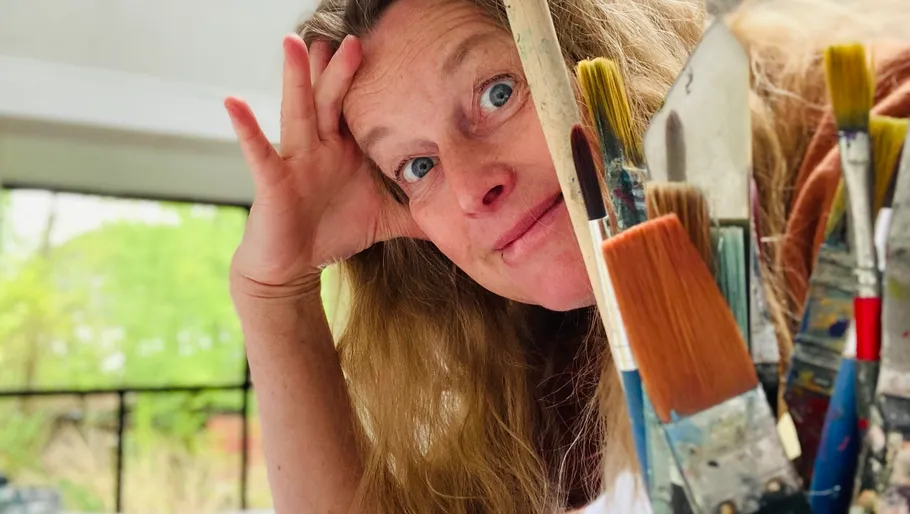Woman with paintbrushes smiling indoors.
