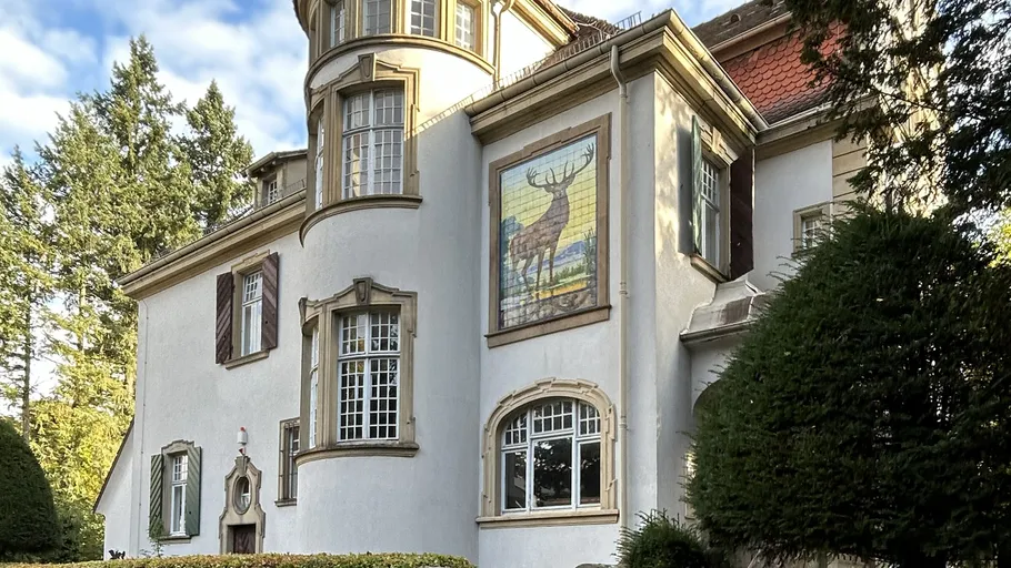 Historisches Gebäude mit Wald und Kunstwerk.