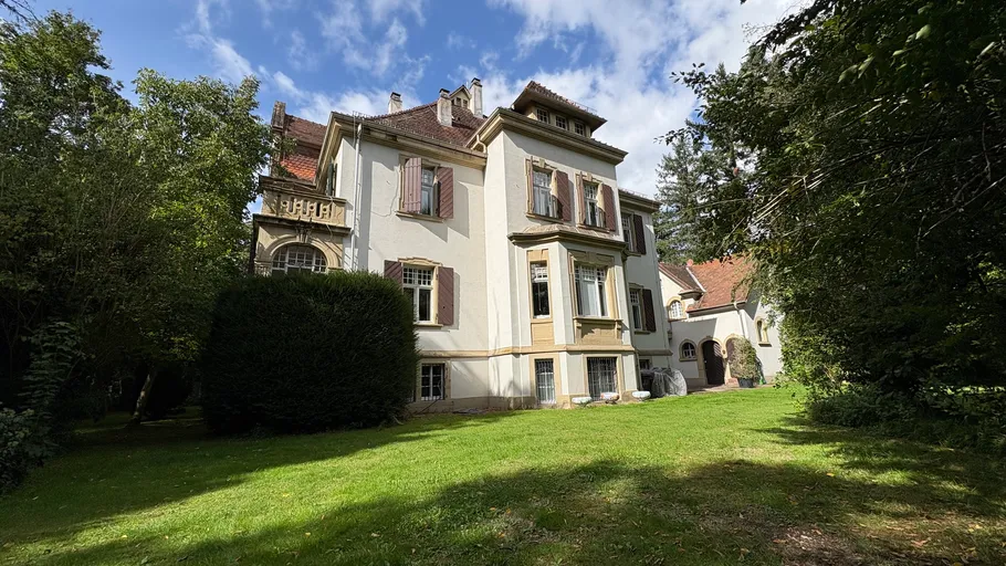 Großes Haus im Garten, teils bewölkter Himmel.