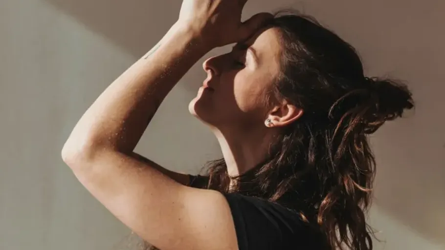 Woman meditating with hand on forehead indoors.