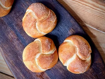 Three brown, sweet rolls on a wooden board.